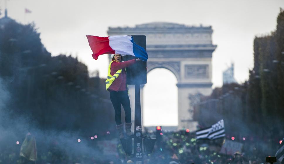 Una joven con el chaleco amarillo ondea una bandera francesa durante la protesta en los Campos Elíseos de París (EFE/EPA/CHRISTOPHE PETIT TESSON)
