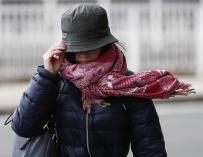 Una mujer sujeta su gorro en Pamplona para impedir que se lo lleve el viento. EFE/Jesús Diges