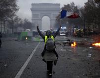 Un manifestante que usa un chaleco amarillo ondea una bandera francesa durante los enfrentamientos con la policía antidisturbios cerca del Arco de Triunfo (EFE/EPA/YOAN VALAT)
