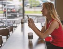 Una mujer toma café mientras mira el móvil