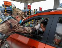 Un militar chino toma la temperatura a un ciudadano en una carretera a las afueras de Wuhan. / EFE