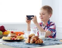 Un niño desayuna mientras juega con un móvil