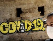 Una persona con mascarilla pasa ante un grafiti este miércoles en Valencia, en el quincuagésimo tercer día del estado de alarma decretado por el Gobierno durante la crisis del Coronavirus. EFE/Ana Escobar