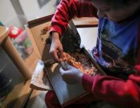 Un niño come un trozo de pizza del menú infantil de Telepizza mientras ve la televisión en su casa. /Jesús Hellín/ Europa Press