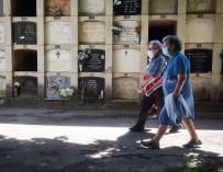 Dos personas protegidas con mascarillas acuden a visitar a sus familiares en el cementerio